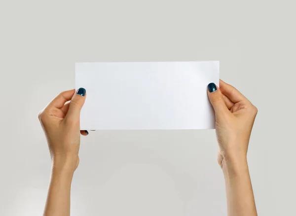 Vrouwelijke handen met een wit vel papier. Geïsoleerd op grijze ba — Stockfoto