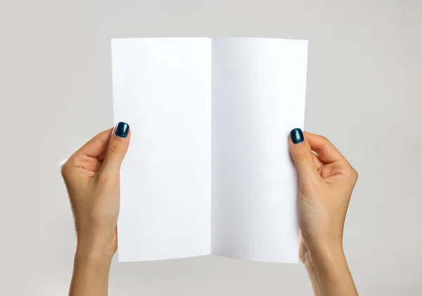 Mãos femininas segurando uma folha branca de papel. Isolado em cinza ba — Fotografia de Stock