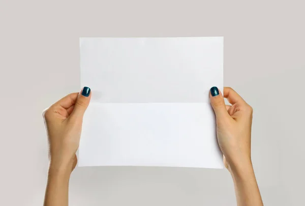 Manos femeninas sosteniendo una hoja blanca de papel. Aislado en ba gris — Foto de Stock