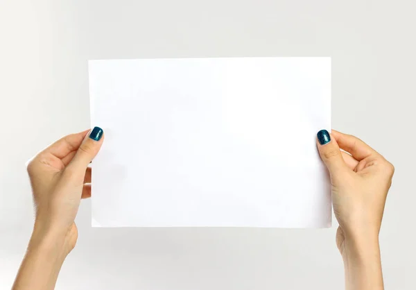 Manos femeninas sosteniendo una hoja blanca de papel. Aislado en ba gris — Foto de Stock