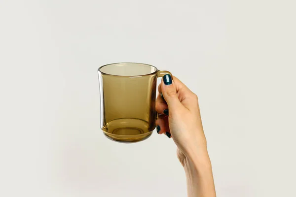 Mão feminina segurando caneca de vidro preto vazio. Isolado nas costas cinza — Fotografia de Stock