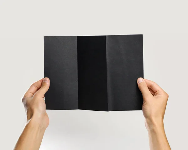 Mãos masculinas segurando um livreto preto folha tripla de papel. Isolado — Fotografia de Stock