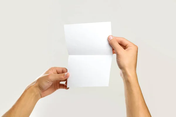 Mężczyzna ręce, trzymając kartkę białego papieru. Na białym tle na szary grzbiet — Zdjęcie stockowe