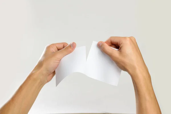 Αρσενικό χέρια rip ένα λευκό φύλλο χαρτί. Απομονωμένα σε γκρι λεμονάτα — Φωτογραφία Αρχείου