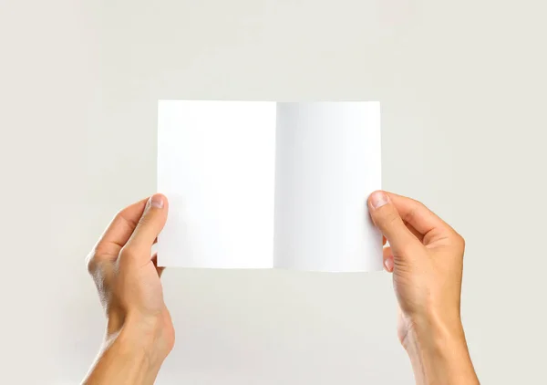 Manos masculinas sosteniendo una hoja blanca de papel. Aislado en la espalda gris — Foto de Stock