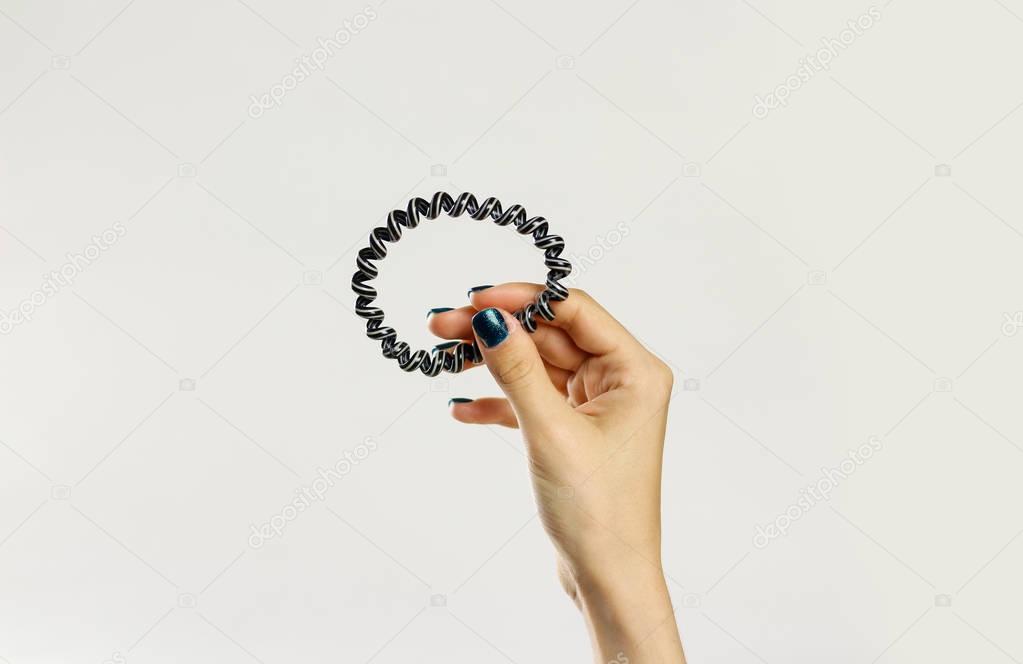 Female hand holding plastic spirally scrunchie. Isolated on gray