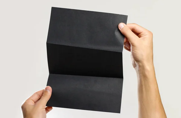 Αρσενικό χέρια κρατώντας ένα μαύρο φυλλάδιο τριπλό φύλλο χαρτιού. Μόνωσ — Φωτογραφία Αρχείου