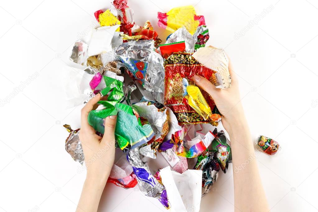 Hands holding a bunch of candy wrappers on a white background. C