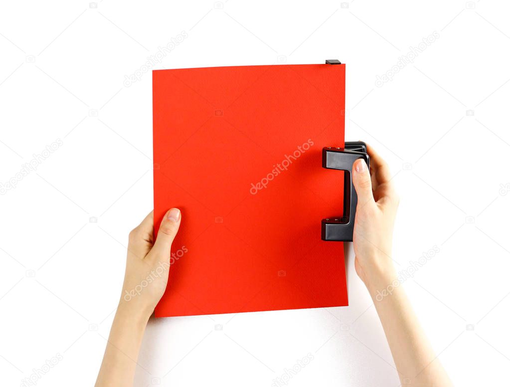 Hands pierce the red paper puncher on a white background. Closeu