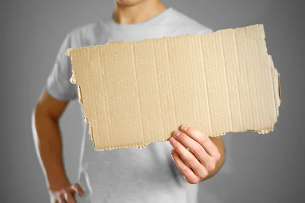 Ένας νεαρός άντρας σε ένα λευκό t-shirt, κρατώντας ένα κομμάτι χαρτόνι. Προ — Φωτογραφία Αρχείου