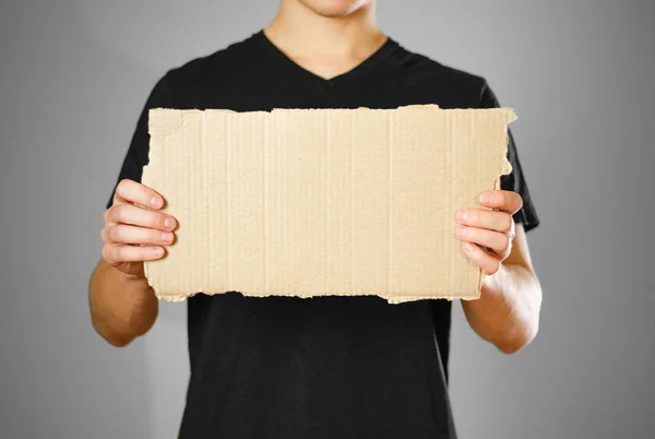 Ένας νεαρός άντρας σε ένα μαύρο t-shirt, κρατώντας ένα κομμάτι χαρτόνι. Προ — Φωτογραφία Αρχείου