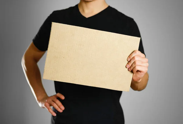 Молодий хлопець у чорній футболці тримає шматок картону. Попередній — стокове фото