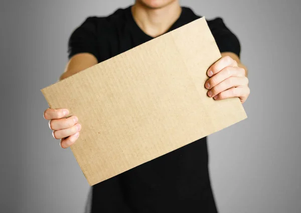 Ein junger Mann in einem schwarzen T-Shirt hält einen Karton in der Hand. vor — Stockfoto