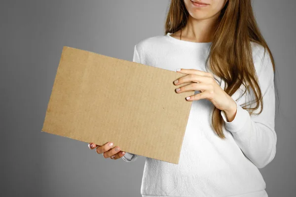 A young girl in a white jacket holding a piece of cardboard. Pre — Stock Photo, Image