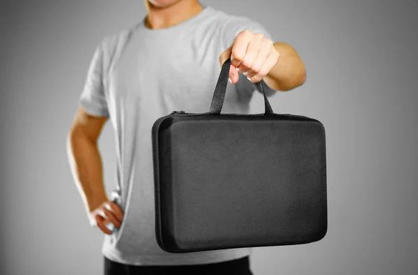 A man in a gray t-shirt holds a black case. Isolated on grey bac — Stock Photo, Image