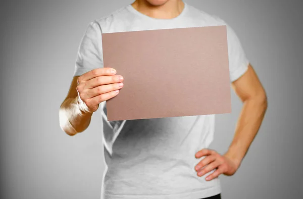 Мужчина в серой футболке держит коричневый чистый лист А4. I — стоковое фото