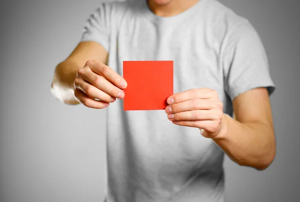 Mężczyzna w szary t-shirt posiada czerwony czysty pusty kwadrat naklejki. — Zdjęcie stockowe