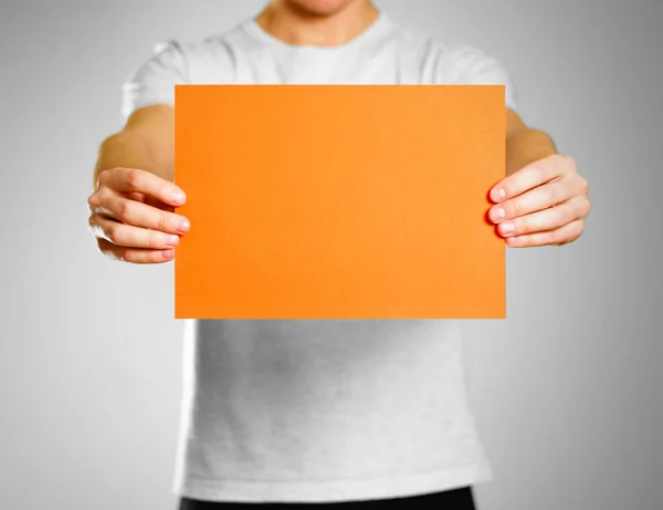 Ein Mann in einem grauen T-Shirt hält ein orangefarbenes weißes Blatt a4. — Stockfoto