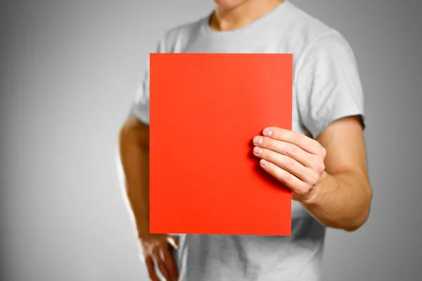 Ένας άντρας σε ένα γκρι t-shirt κρατά ένα κόκκινο καθαρό κενό φύλλο Α4. ISO — Φωτογραφία Αρχείου