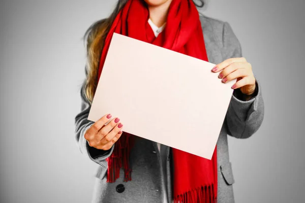 Una chica con abrigo gris y bufanda roja mantiene un beige limpio en blanco shee — Foto de Stock