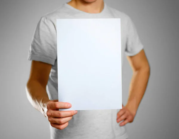 Um homem em uma camiseta cinza mantém uma luz azul limpa folha em branco de — Fotografia de Stock