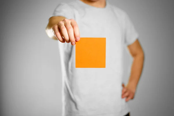 Un hombre con una camiseta gris sostiene una pegatina cuadrada vacía de color naranja —  Fotos de Stock