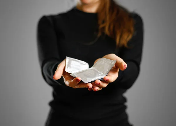 La chica de la mano sostiene un preservativo. De cerca. Aislado sobre fondo gris —  Fotos de Stock