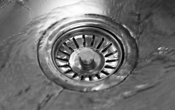 Water flows into the middle of a metalic sink. Close up