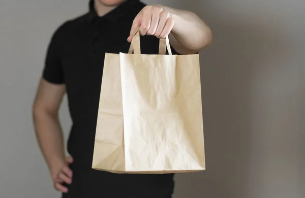 Ένας άντρας κρατάει μια χάρτινη σακούλα. Κλείσε. Απομονωμένο σε γκρι φόντο — Φωτογραφία Αρχείου
