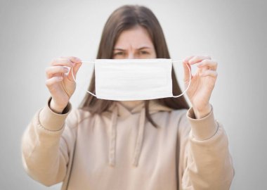 Kızın elinde tıbbi bir maske var. Kapatın. Gri bir arkaplanda izole edilmiş.