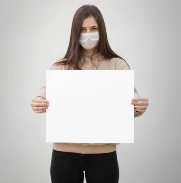 医療用マスクの少女は空の白い紙を持っている 閉めろ 灰色の背景に隔離された — ストック写真