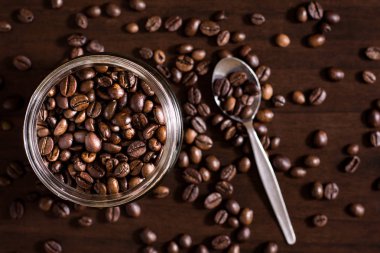 Kavrulmuş kahve çekirdekleri kaşık ile ahşap masa üzerinde kavanoz.