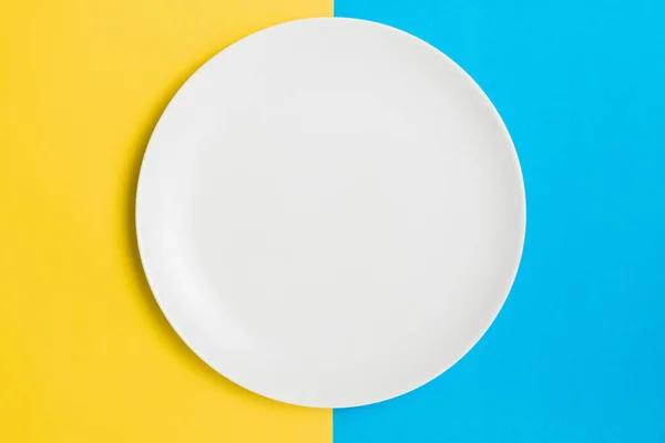 Empty round plate on a contrasting yellow and blue background. — Stock Photo, Image