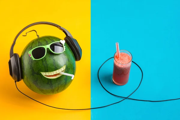 Cara de melancia feliz ouvindo música com fones de ouvido e copo de suco . — Fotografia de Stock