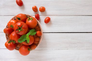 Dokuma sepetindeki çiğ organik domatesler yazı için kopyalama alanı olan beyaz masanın üzerinde yatıyordu.