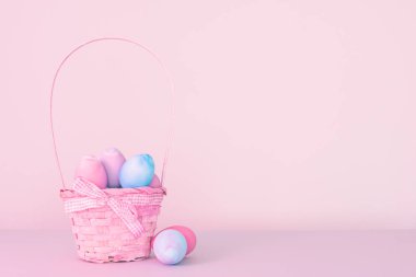 Pastel pembe ve mavi Paskalya yumurtaları pembe arka planda dokuma sepetinde - Paskalya tatili konsepti resmi fotokopi alanı ile.