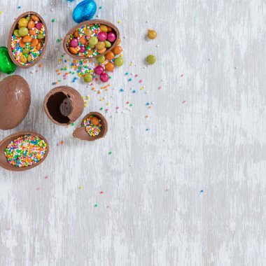 Çikolatalı paskalya yumurtaları ve beyaz ahşap masa üstündeki diğer şekerler - kare 1x1 bayramlar ve metin için fotokopi alanı ile kutlama konsepti imajı.