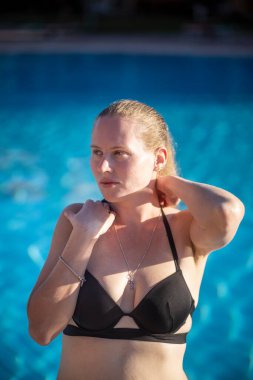 Mavi havuzun arka planında siyah mayo giymiş bir kadının güzel portresi. Öğleden sonra vuruldu..