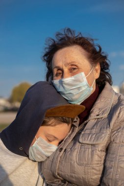 Yaşlı bir kadın ve mavi tıbbi maskeli bir gencin portresi. Mavi gökyüzüne karşı portre. Üzgünler. Covid 19.