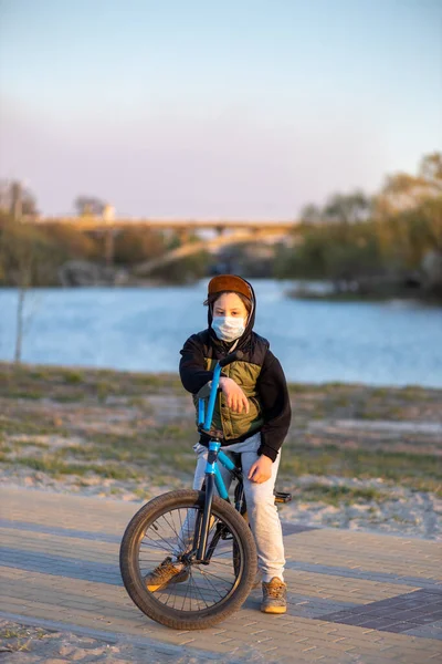 Portrait of a teenager in the sunset in a mask on a blue bicycle. Quarantine. It is forbidden to ride a bicycle. Covid-19.