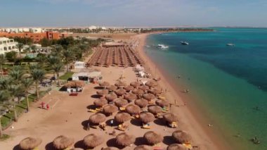 Güzel kumlu sahil, masmavi şeffaf deniz. İnsanlar Kızıl Deniz 'de banyo yapıyor. İnsanlar sahilde dinleniyor. Turistler dinleniyor. Yeşil palmiye ağaçları. Turistler için tekneler.