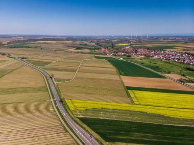 Yukarıdan güzel sarı kolza tohumu tarlası. Yeşil alanlar. Üzüm tarlaları. Küçük bir Alman köyü. Güzel mavi gökyüzü. Rüzgar tarlaları.