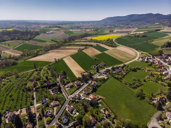 Top view of different fields near the French town of Wissembourg. Green, yellow and gray plowed fields. Mountains in the background. Different houses and roads.