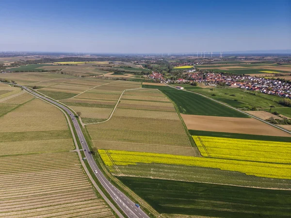 Yukarıdan güzel sarı kolza tohumu tarlası. Yeşil alanlar. Üzüm tarlaları. Küçük bir Alman köyü. Güzel mavi gökyüzü. Rüzgar tarlaları.