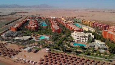 Otelin üstünden ve Hurghada yakınlarındaki çölden uçuyor. Konut manzarası, turistler için yüzme havuzları. Çölün ortasında güzel bir bölge. Oasis. Sahilin üst manzarası, sahil, kristal berrak deniz. Mısır.