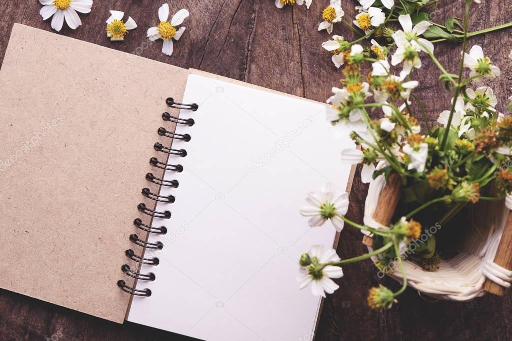 Blank notebook with white flower and bas ket of flower on vintage wooden table View from above with copy space
