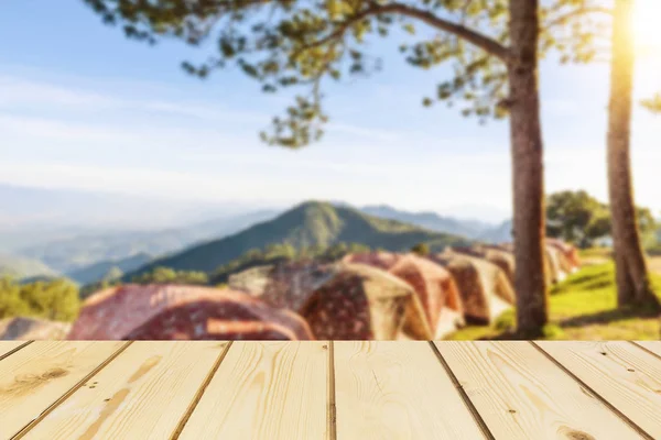Tavola di legno tavolo vuoto di fronte a sfondo sfocato di tenda per il campeggio in montagna con pini e mare di nebbia e bagliore utilizzato per modellare per visualizzare o montare i vostri prodotti, vintage . — Foto Stock