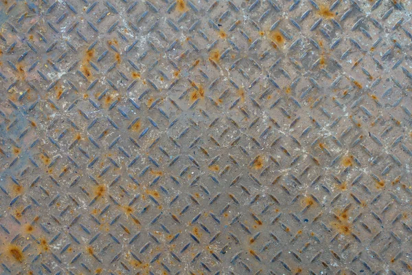 Old metal floor plate with diamond pattern and rusty background texture.