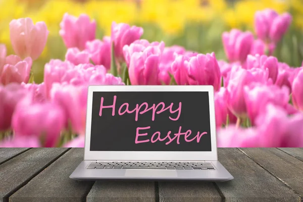 Чистый ноутбук компьютер на деревянном столе и цветок тюльпана подается сад в утреннем солнечном свете на Пасхальный праздник или макет вашего продукта отображения — стоковое фото