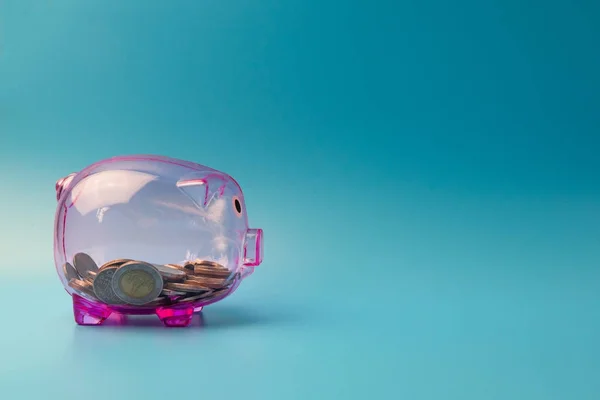 Σαφή ροζ κουμπαράς σε μπλε φόντο με κέρματα για εξοικονόμηση m — Φωτογραφία Αρχείου